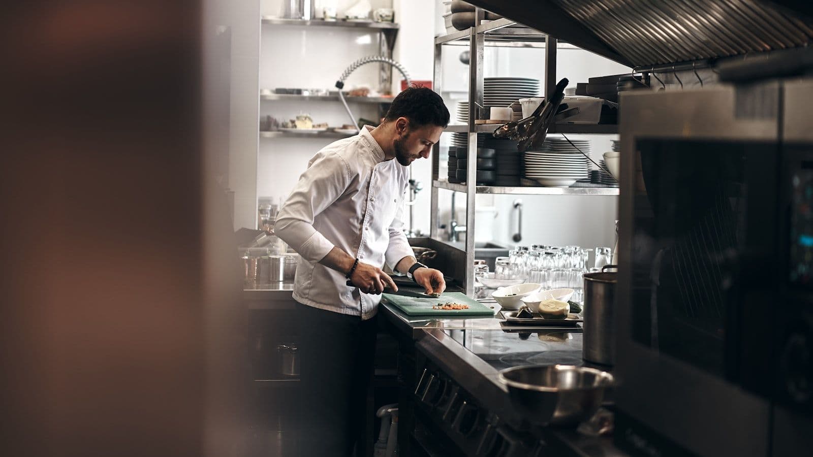 Chef en cuisine de restaurant indépendant en train de dresser une assiette, filmé en plan rapproché
